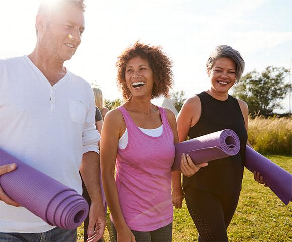 Three people walking in field with Pilates mats for group session